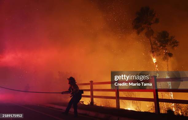 Firefighter pulls a water hose as the Franklin Fire burns palm trees near a building on December 10, 2024 on Malibu, California. The wildfire has...