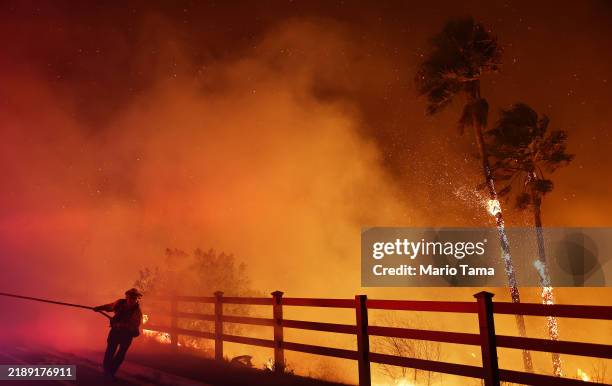Firefighter pulls a water hose as the Franklin Fire burns palm trees near a building on December 10, 2024 in Malibu, California. The wildfire has...