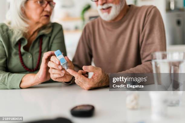 senior couple using lancet on finger for checking blood sugar level by glucose meter, healthcare and medical, diabetes, glycemia concept - glycemia stock pictures, royalty-free photos & images