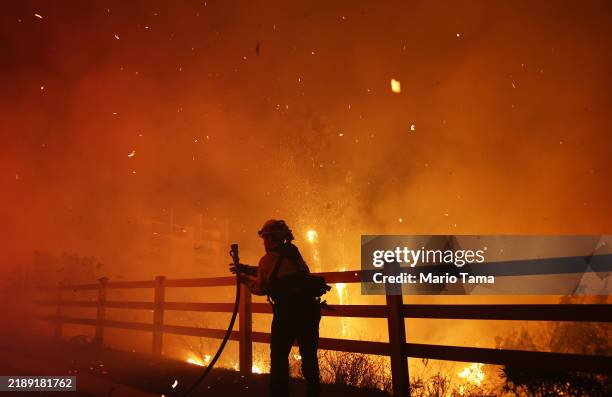 Firefighter pulls a water hose as the Franklin Fire burns near a building on December 10, 2024 in Malibu, California. The wildfire has scorched 1,800...