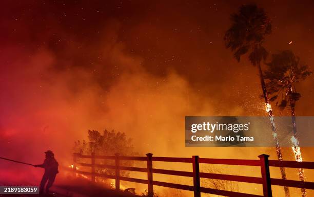 Firefighter pulls a water hose as the Franklin Fire burns palm trees on December 10, 2024 n Malibu, California. The wildfire has scorched 1,800 acres...