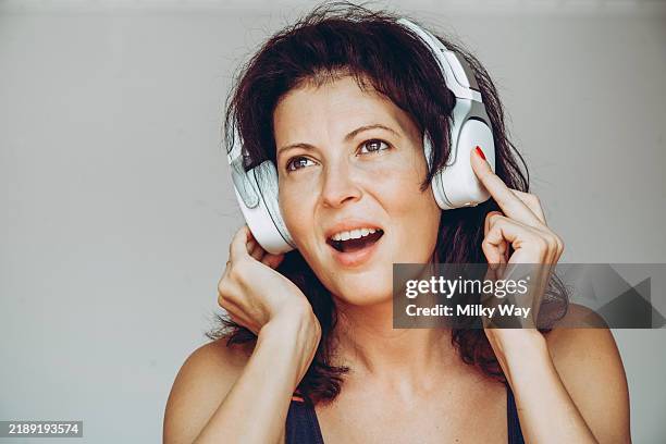 brunette white woman wearing white headphones listens to music and looks surprised or amazed. close-up portrait. - begleitgesang stock-fotos und bilder