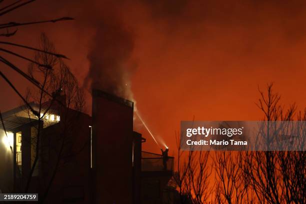 Firefighter sprays water as firefighters work to protect a home while the Franklin Fire burns on December 10, 2024 n Malibu, California. The wildfire...