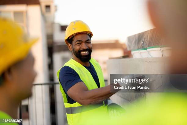 happy construction worker smiling while applying plaster to wall - dakdekker stockfoto's en -beelden