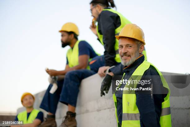 smiling construction workers in safety gear taking a break on site - operário siderúrgico imagens e fotografias de stock