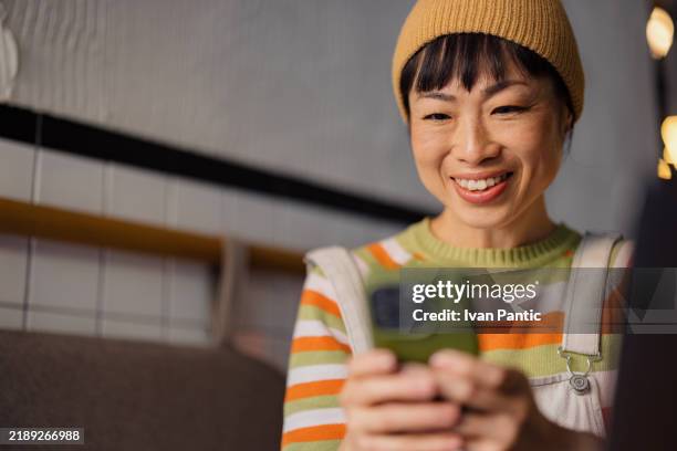 smiling woman using smartphone in cozy coffee shop setting - welvaart stockfoto's en -beelden