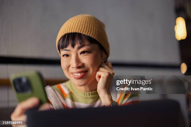 frau lächelt, während sie ihr smartphone am cozy cafe workspace benutzt - warmes licht stock-fotos und bilder