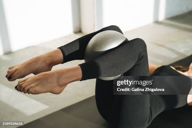 young slim woman in sportswear doing pilates stretching on mat with ball in modern studio - swiss ball stock pictures, royalty-free photos & images