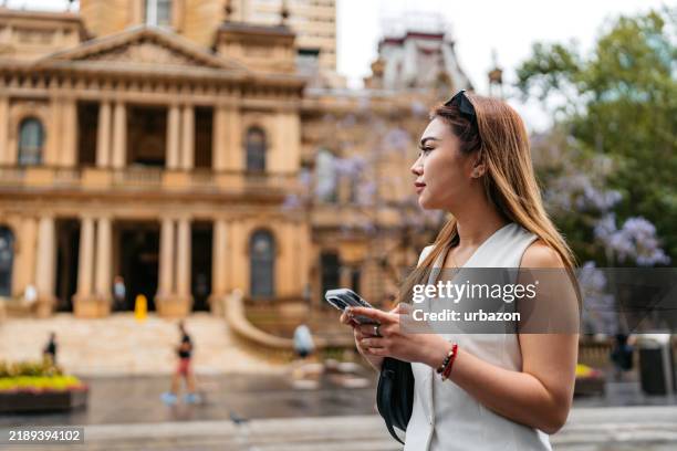 young asian woman using phone near sydney town hall in sydney in australia - local government building stock pictures, royalty-free photos & images