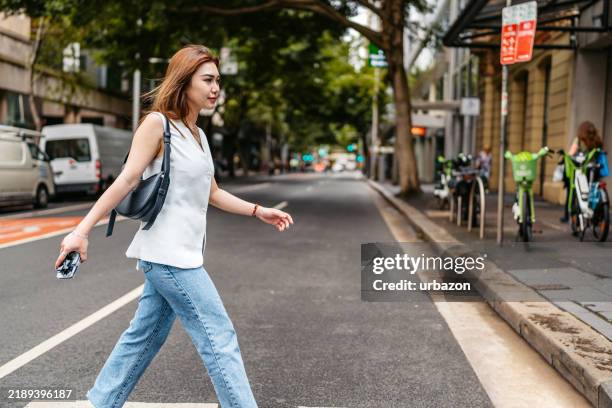 young asian woman crossing the street in sydney in australia - pedestrian stock pictures, royalty-free photos & images