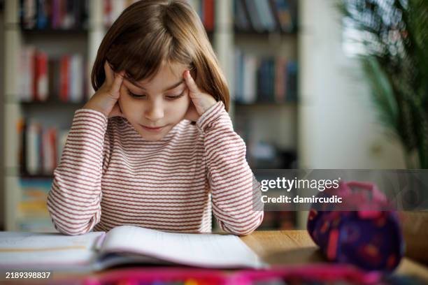 scolaretta che si sente distratta mentre studia a casa, tiene la testa e guarda le pagine del libro - dislessia foto e immagini stock
