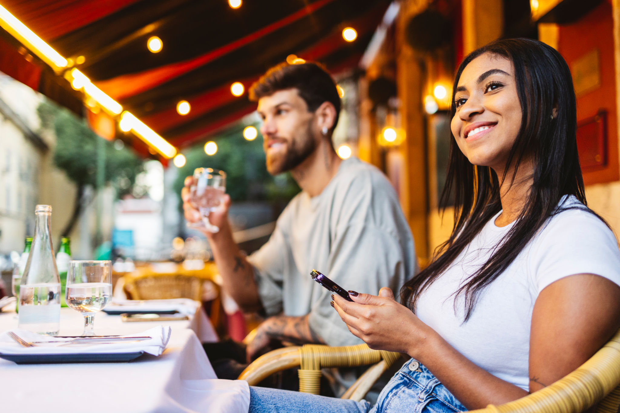 Young woman using phone while enjoying dinner with friend at outdoor restaurant in lisbon Young woman using phone while enjoying dinner with friend at outdoor restaurant in lisbon