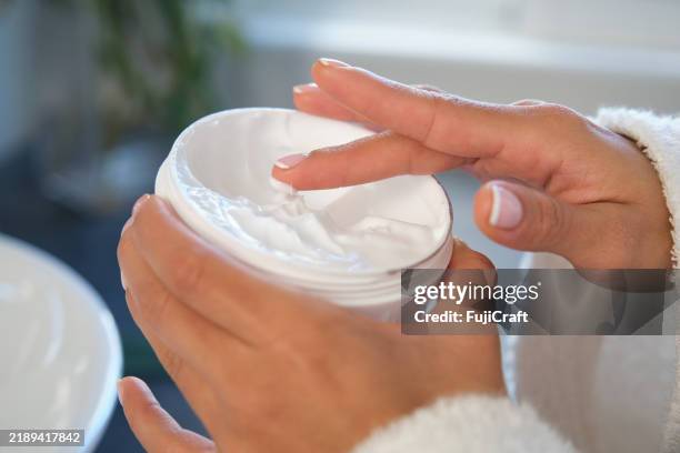 donna che applica una crema idratante a casa - crema idratante foto e immagini stock
