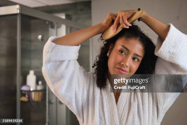 young woman brushing curly hair in bathroom after shower - brushing stock pictures, royalty-free photos & images