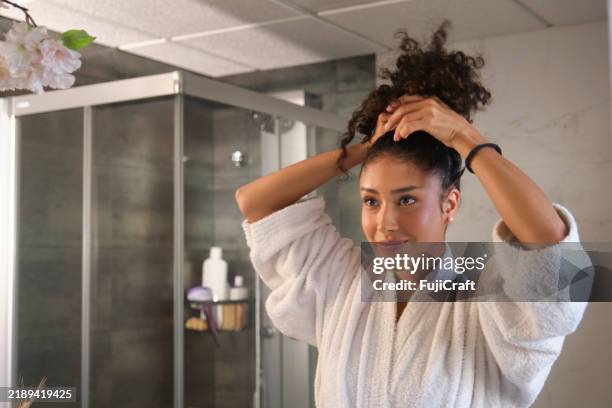 young woman tying her hair in a modern bathroom - hair back stock pictures, royalty-free photos & images