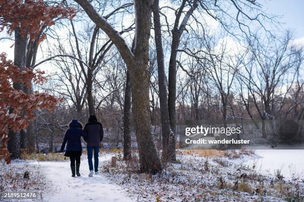 una pareja camina hacia un puente de piedra en un parque en un día frío y nevado de invierno, minnesota - rochester minnesota fotografías e imágenes de stock
