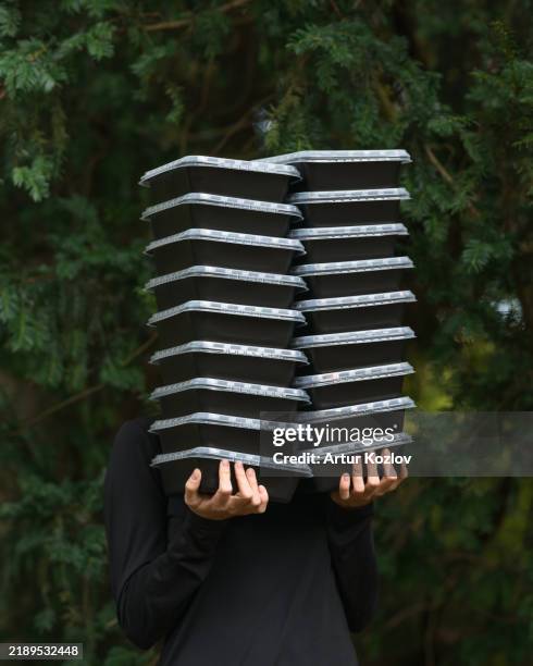 stack of plastic food containers in hands on green background. microwave meal prep. black plastic tray with transparent lid for food storage and packaging. food delivery. lunch boxes. plastic concept. - ciotola vuota foto e immagini stock