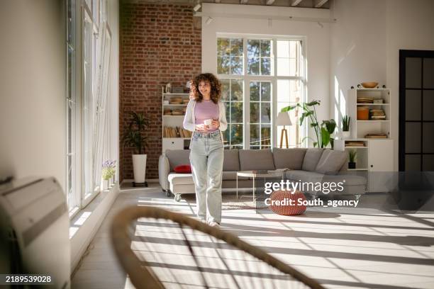 woman enjoying coffee in a cozy, modern living room with natural light - hygge stock pictures, royalty-free photos & images