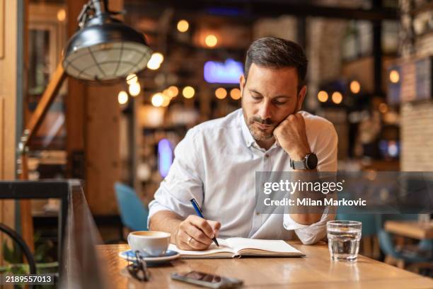 hombre de negocios en una cafetería - bebiendo café y escribiendo ideas - un solo hombre fotografías e imágenes de stock