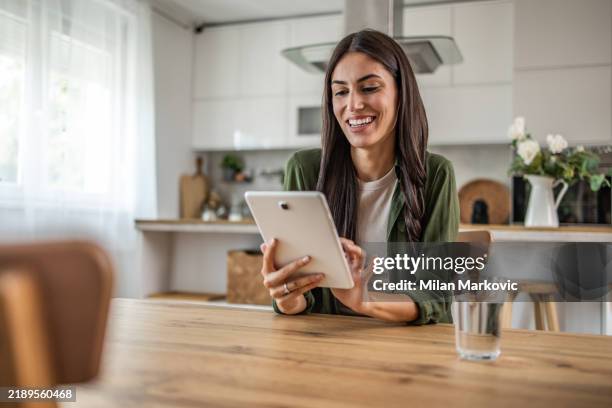 smiling young woman using digital tablet while sitting at table in dining room - ipad bildbanksfoton och bilder