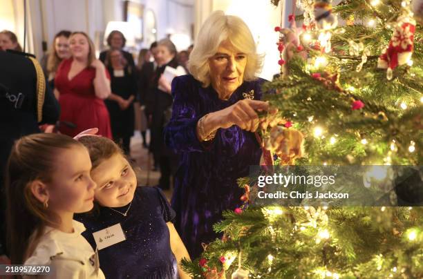 Queen Camilla and young guests decorate a Christmas tree in the Library as she welcomes children and families supported by Helen & Douglas House and...