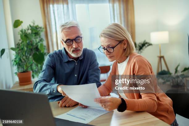 pareja madura revisando facturas en casa - plan financiero fotografías e imágenes de stock