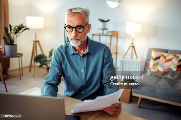 mature man going over bills at home - kontoauszug stock-fotos und bilder