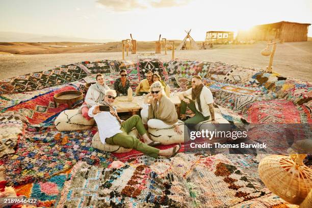 wide shot senior man taking selfie of friends and family at desert camp - morocco stock pictures, royalty-free photos & images