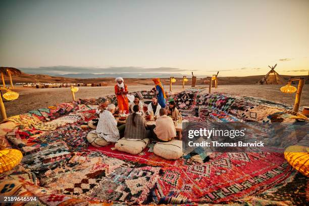 wide shot friends sharing sunset dinner at moroccan desert camp - voyage expérientiel photos et images de collection