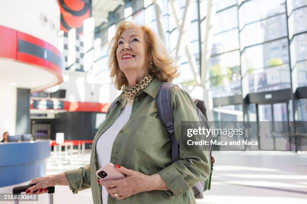 senior woman at a modern transit hub carrying smartphone and luggage - só uma mulher idosa imagens e fotografias de stock