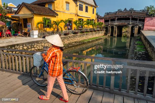 vietnamese woman crossing streets in an old town of hoi an city, vietnam - hoi an stock pictures, royalty-free photos & images