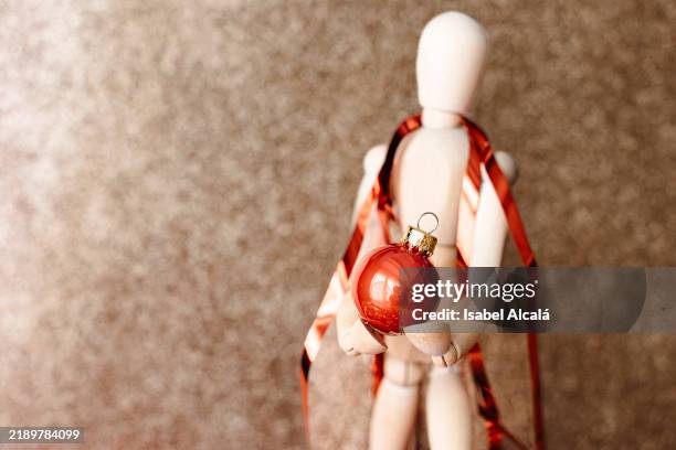wooden figure holding red christmas bauble with ribbon - maniquí fotografías e imágenes de stock