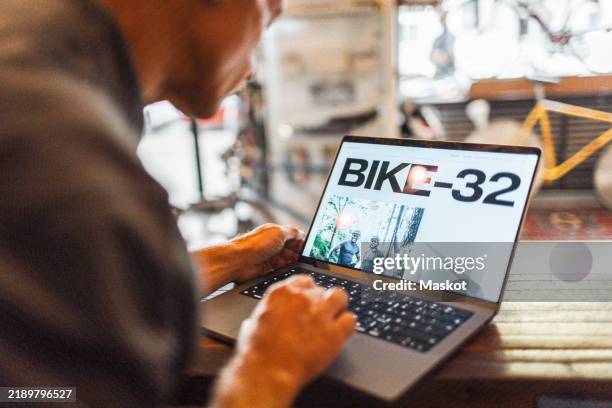 over the shoulder view of male owner using laptop on checkout counter at bicycle shop - über die schulter stock-fotos und bilder