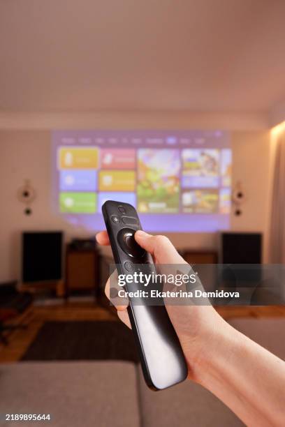 hand holding remote control, projecting multimedia content on wall in living room - video on demand foto e immagini stock
