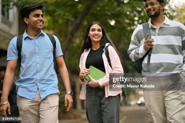 jeunes hommes et étudiantes joyeux avec des sacs à dos marchant sur le campus universitaire - bâtiment public photos et images de collection