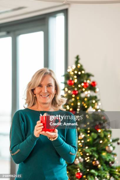 joyful mature caucasian woman savoring coffee in festive office - decorating the christmas tree stock pictures, royalty-free photos & images