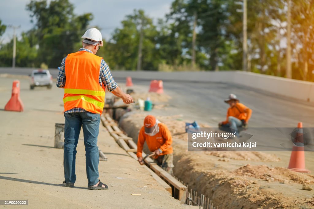 Senior Asian engineer supervises and inspects road construction at the construction site.