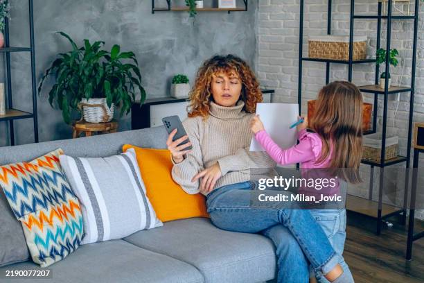 mother with smartphone ignoring her daughter in living room - negeren stockfoto's en -beelden