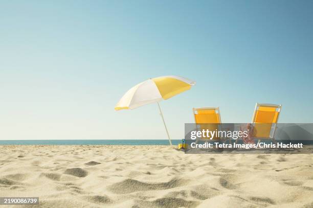 two yellow beach chairs and umbrella on sandy beach facing ocean - strandschirm stock-fotos und bilder