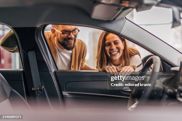 a couple looking inside a new car at the dealership. - honda dealer stock pictures, royalty-free photos & images