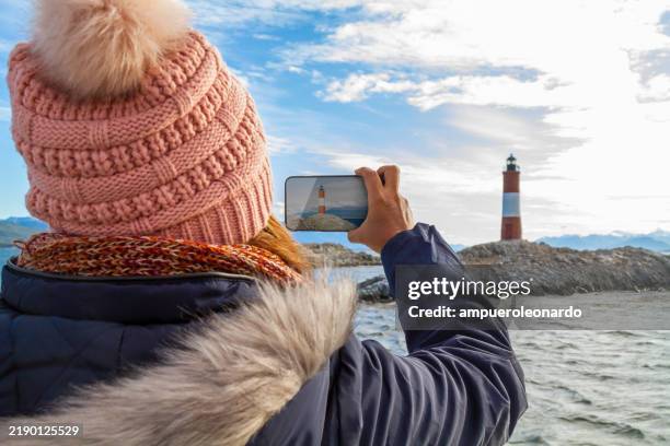 afro mature backpacker stylish female tourist photo of les eclaireurs lighthouse in the beagle channel, ushuaia, tierra del fuego, patagonia, argentina, latin america with her smartphone using 5g technology. - tierra del fuego province chile stock pictures, royalty-free photos & images