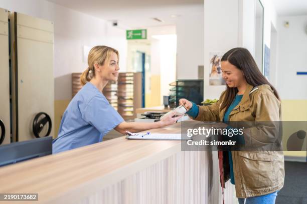 smiling veterinary receptionist assisting client with payment - veterinary receptionist stock pictures, royalty-free photos & images