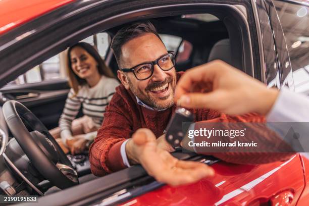 a couple sitting in a car, receiving the keys from a car dealer - car rental stock pictures, royalty-free photos & images