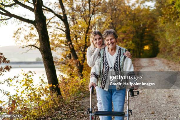 nurse and female senior patient with rollator on walk in autumn nature. elderly care and home caregiver concept. - osteoporose stock-fotos und bilder