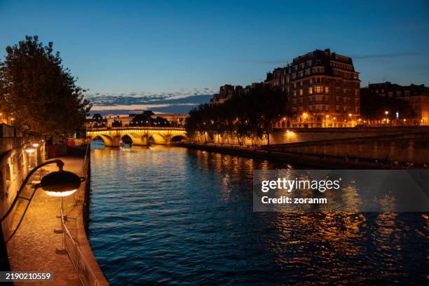 illuminated arched bridge and riverbanks on the seine river at dusk in paris, france - uitzicht-over-stadje stockfoto's en -beelden