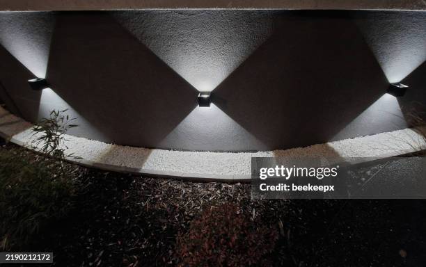 spot wall light illuminates the wall of facade of the house in a conical shape at night. evening positioning and navigation lamp of black color shines in two directions on the gabion wall, back yard