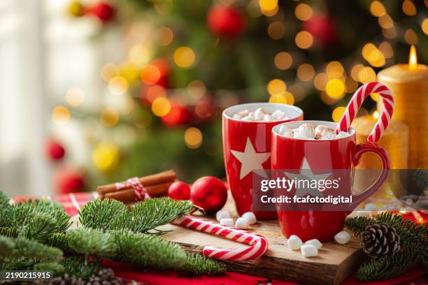 two hot chocolate marshmallow mugs and christmas decoration near illuminated christmas tree - mug stock pictures, royalty-free photos & images