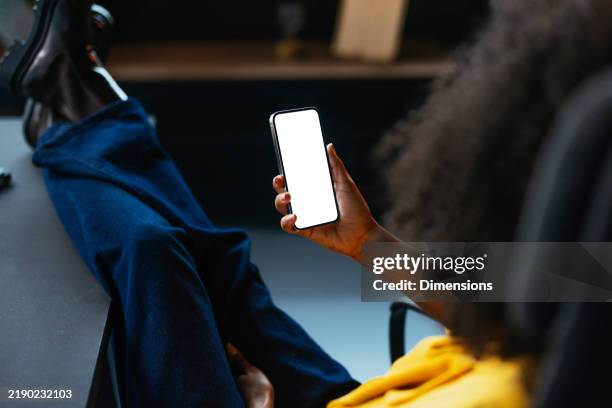 businesswoman relaxing with feet up on desk and browsing smartphone - dark skin tone stock pictures, royalty-free photos & images