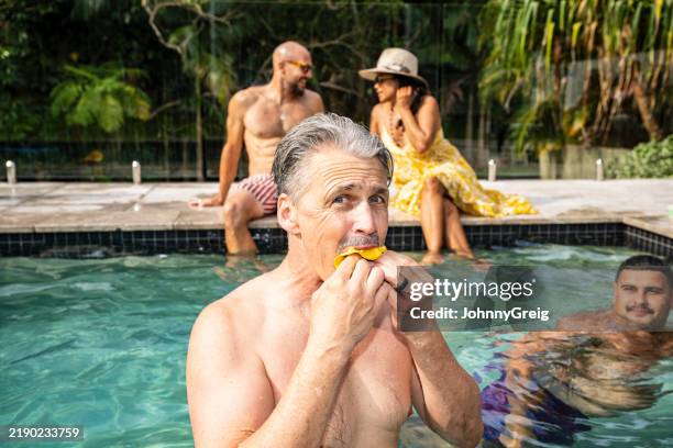 mature man standing in swimming pool and eating mango fruit - mango fruit stock pictures, royalty-free photos & images