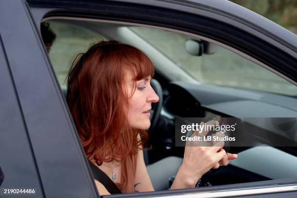 a woman is sitting in a car checking her smartphone with focus and attention - car instagram stock pictures, royalty-free photos & images